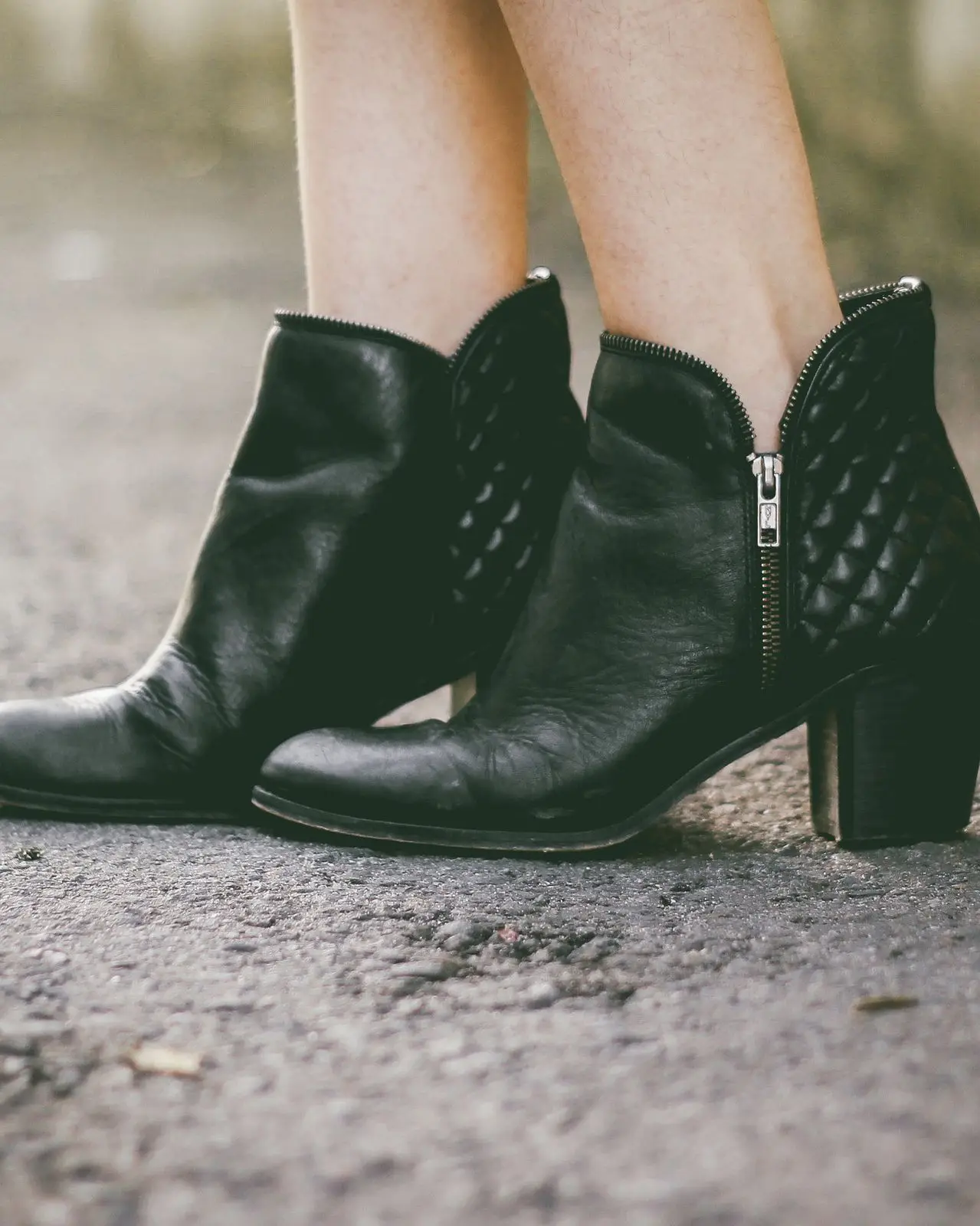 Black leather ankle boots with quilted panels and a block heel on a gravel path