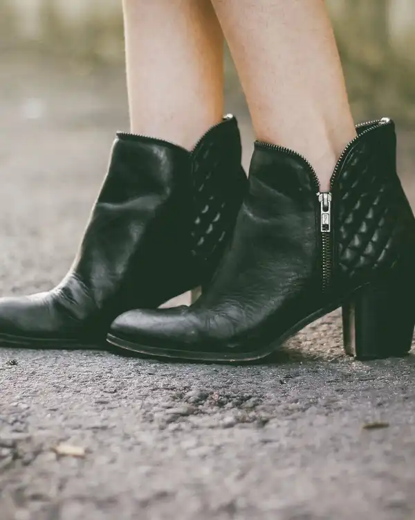 Black leather ankle boots with quilted panels and a block heel on a gravel path