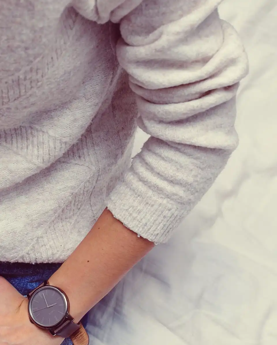 A close view of a pale cable-knit jumper worn with blue jeans and a dark watch